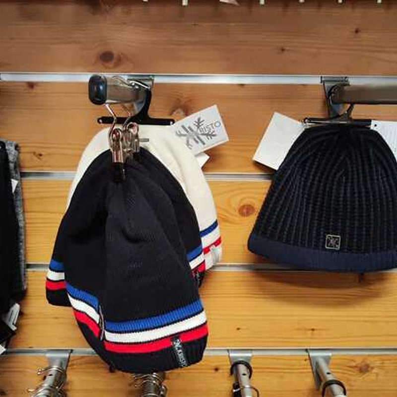 Bonnets RISTO d'hiver : modèles à rayures tricolores. Présentation de bonnets RISTO sur lattes de bois : un modèle noir et un blanc avec rayures tricolores (rouge, blanc, bleu), et un bonnet côtelé noir.