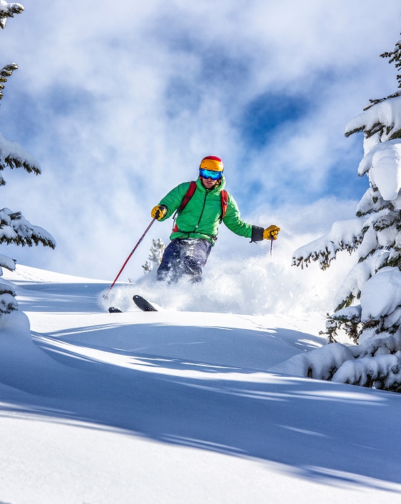 Poudreuse épique : Skieur en action sous le soleil de montagne. Skieur en veste verte descendant rapidement une montagne, soulevant un jet de poudreuse dense sous le soleil.