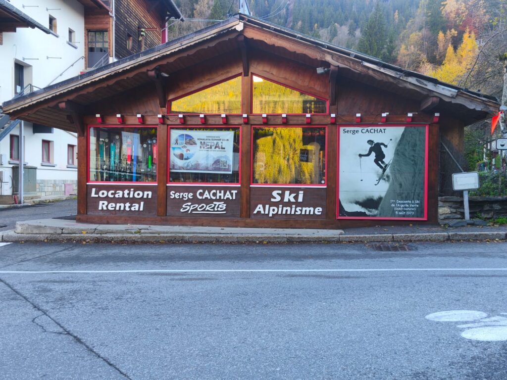 Serge CACHAT Sports: Location, Ski Alpinisme et légende. Kiosque Serge CACHAT SPORTS (Location Rental, Ski Alpinisme) en bois. Une affiche historique montre la 1ʳᵉ Descente à ski de l'Aiguille Verte (1973).